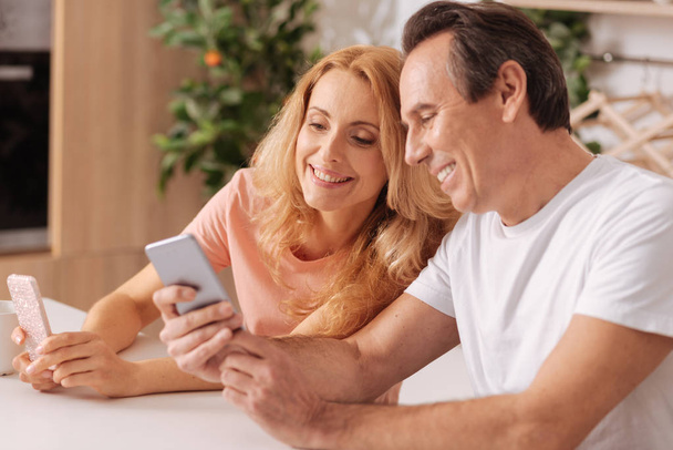 Positive mature couple using digital smartphones at home - Zdjęcie, obraz