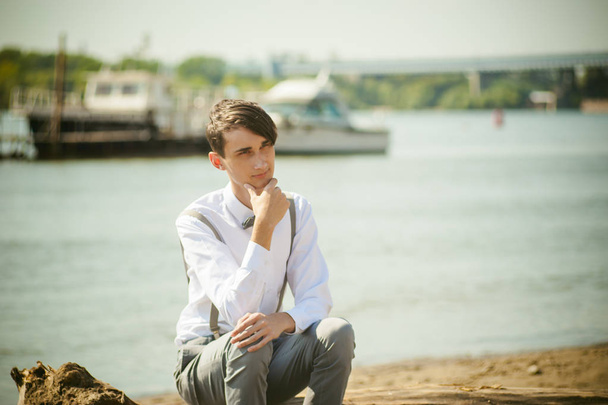 young skinny man, elegantly stylishly dressed in white shirt, trousers with suspenders and bow tie - 写真・画像