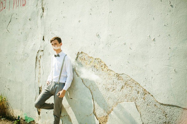 young skinny man, elegantly stylishly dressed in white shirt, gray trousers with suspenders and bow tie - 写真・画像
