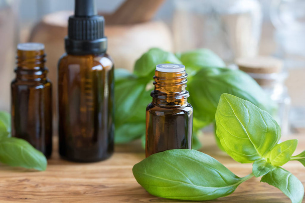 A bottle of basil essential oil with fresh basil leaves - Фото, зображення