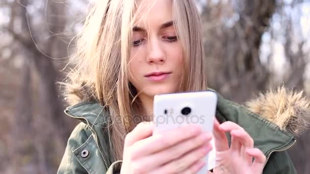 Όμορφη κοπέλα με μακριά ξανθά μαλλιά γράφοντας ένα μήνυμα στο τηλέφωνο - Πλάνα, βίντεο