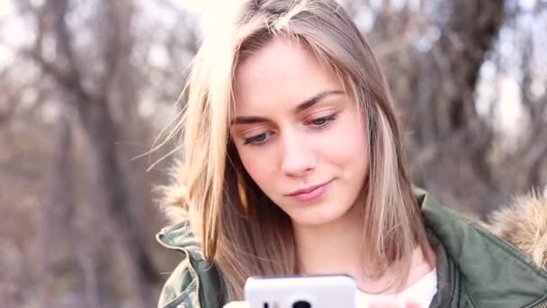 Menina jovem e bonita com cabelo loiro está segurando um telefone e está escrevendo uma mensagem
 - Filmagem, Vídeo
