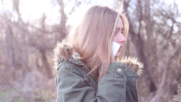 Young beautiful woman with blond hair is talking on the phone in park - Footage, Video