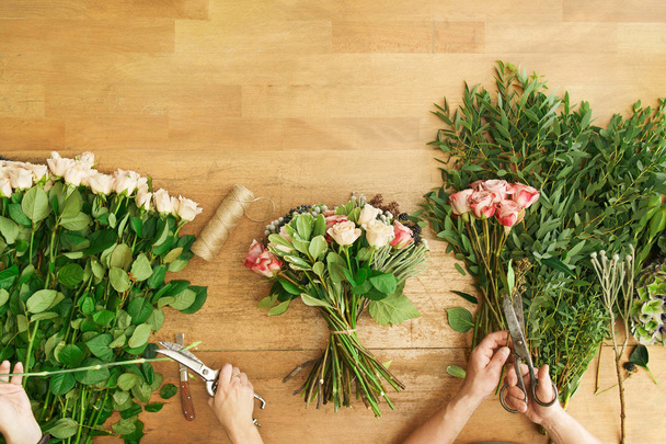 Florist and assistant in flower shop delivery make rose bouquet, table top view - Photo, Image