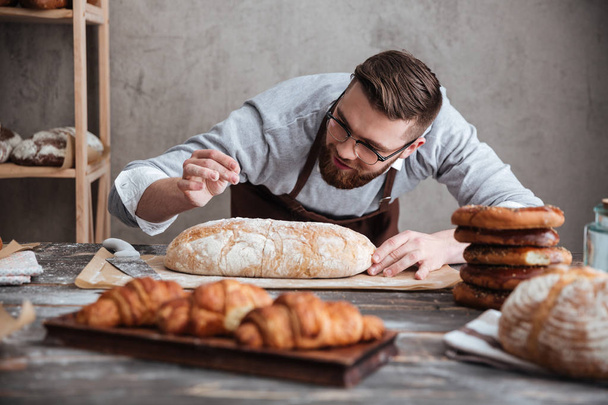 Концентрированный человек пекарь, стоящий в пекарне возле хлеба
. - Фото, изображение
