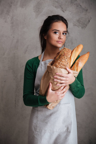 Young cheerful lady baker standing and holding bread. - Foto, Imagem