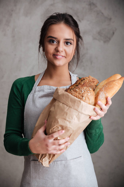Happy lady baker standing and holding bread. - Фото, изображение