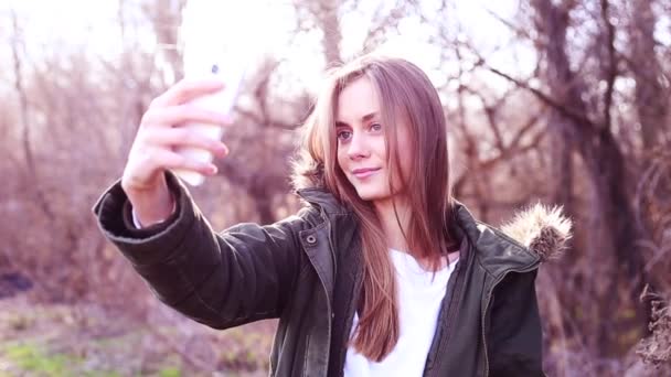 Jovem europeia com cabelo loiro vestido com uma jaqueta e tirar uma selfie no parque e depois de carregado para um site de mídia social
 - Filmagem, Vídeo
