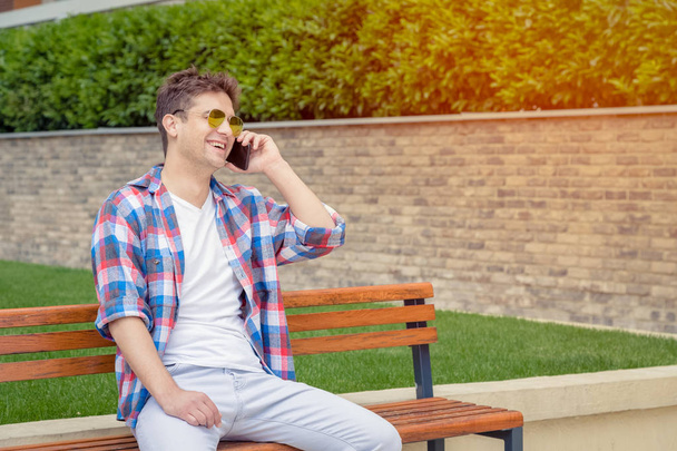 Young man sitting on bench and using smartphone in the park  - Photo, image