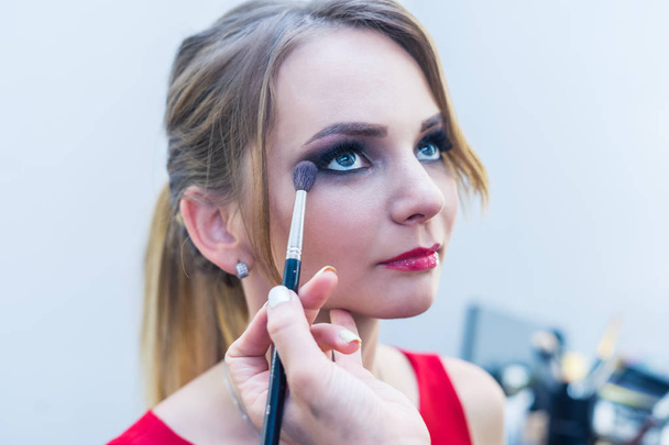 Visagist rokerige ogen make-up doen om mooi jong meisje - Foto, afbeelding