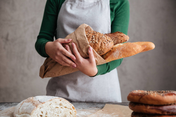 Cropped image of  female baker holding bag with bread  - Zdjęcie, obraz