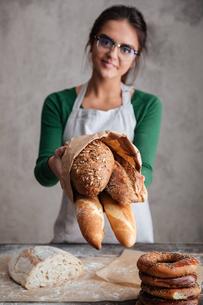 Vertical image of female baker showing bag with bread - Foto, afbeelding
