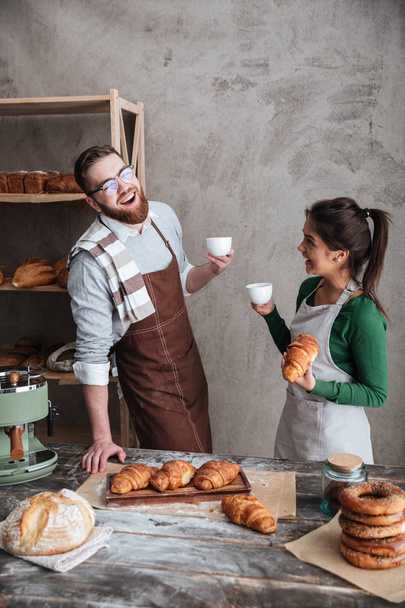 Cheerful loving couple bakers drinking coffee. Looking aside. - Foto, imagen