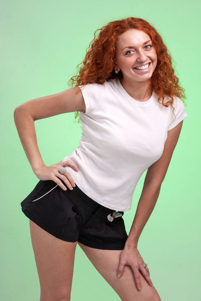 red-haired woman in little shorts, isolated on green - Foto, imagen