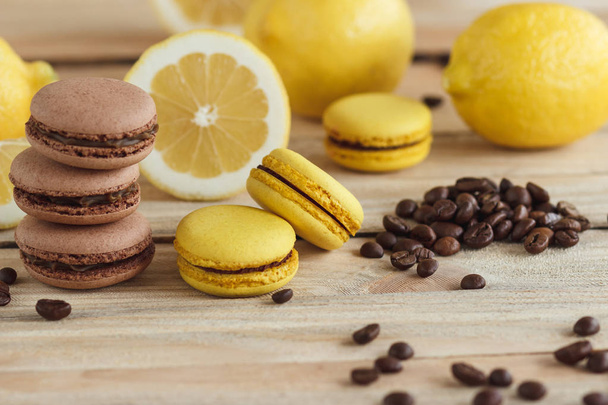 Yellow and brown french macarons with lemons and coffee beans on the wooden board - Photo, Image