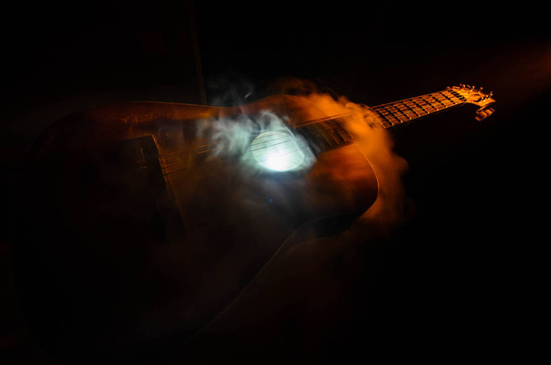 Музична концепція. Акустична гітара ізольована на темному фоні під промінь світла з димом з копіювальним простором. Гітарні струни, крупним планом. Вибірковий фокус. Пожежні ефекти
 - Фото, зображення
