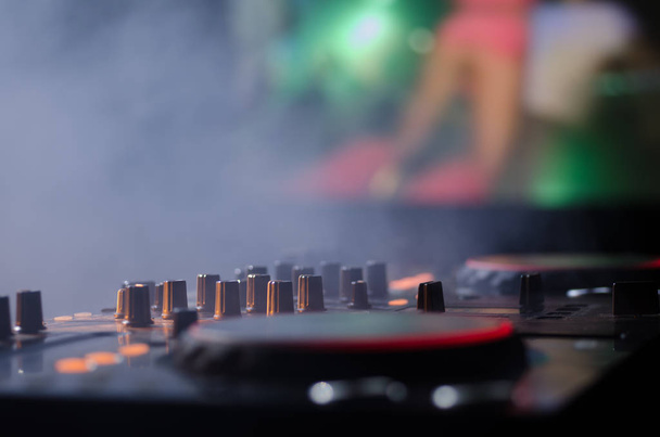 DJ Spinning, Mixing, and Scratching in a Night Club, Manos de dj ajustar varios controles de pista en la cubierta de dj, luces estroboscópicas y niebla, enfoque selectivo
 - Foto, imagen