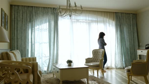 Aufgebrachte Frau geht am Fenster einer gemütlichen Wohnung hin und her - Filmmaterial, Video