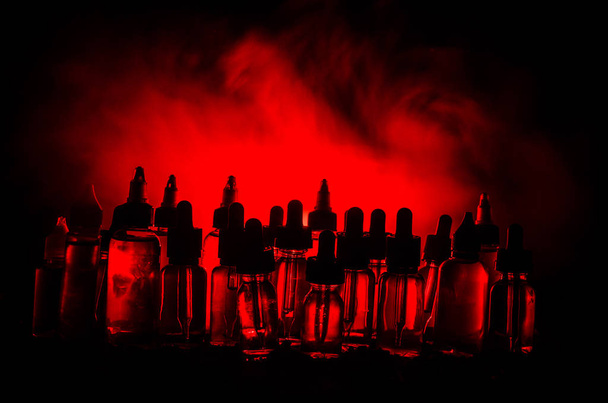 Концепція вейпу. Димові хмари та вейп-рідкі пляшки на темному тлі. Світлові ефекти
. - Фото, зображення