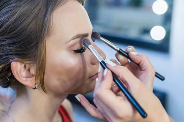 Visagist rokerige ogen make-up doen om mooi jong meisje - Foto, afbeelding