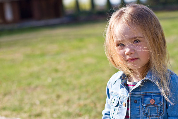 Beautiful charming little girl in jeans with disheveled hair on a background of green - Foto, immagini