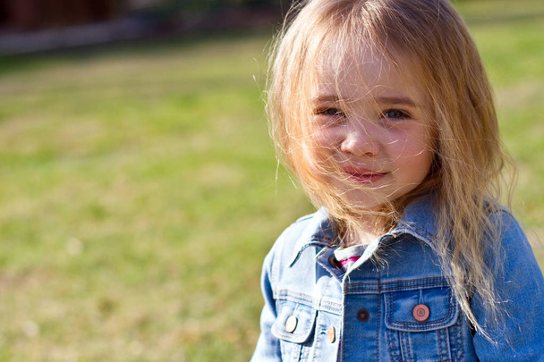 Beautiful charming little girl in jeans with disheveled hair on a background of green - Photo, Image