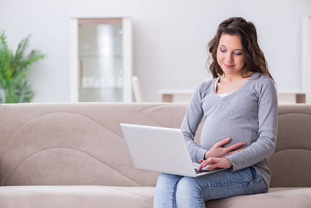 Terhes nő dolgozik laptop ül a kanapén - Fotó, kép