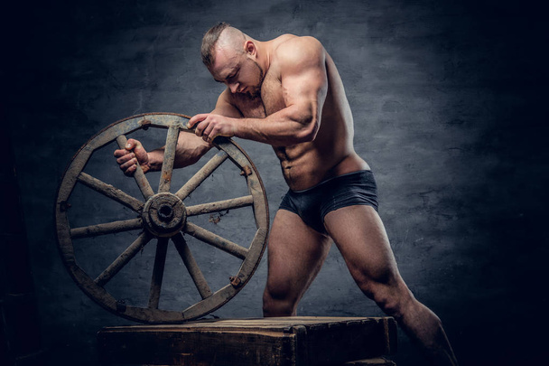 Bodybuilder holds old wooden wheel  - Foto, Imagem