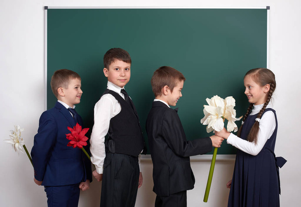 хлопчики дарують дівчині квіти, дитина початкової школи біля порожнього крейдяного фону, одягнена в класичний чорний костюм, груповий учень, концепція освіти
 - Фото, зображення