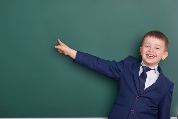 学校の男の子は空白黒板背景、古典的な黒のスーツ、グループの生徒、教育概念に身を包んだ近く指を指す - 写真・画像