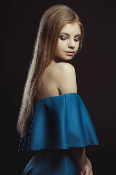 Όμορφη νεαρή γυναίκα με μακριά ξανθά μαλλιά και μπλε φόρεμα με  - Φωτογραφία, εικόνα