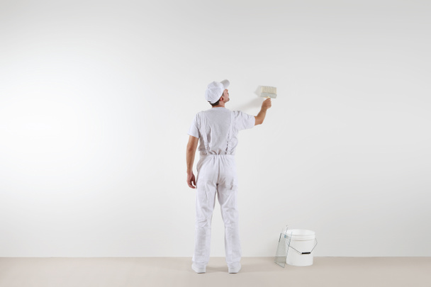 Visão traseira do homem pintor olhando para a parede em branco, com pincel
 - Foto, Imagem