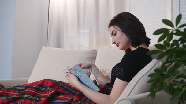 Attractive young woman lying on couch and reading book - Video