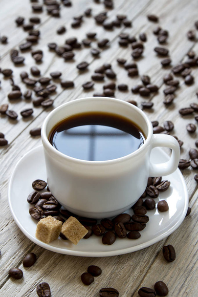 schwarzer Kaffee in einer weißen Tasse und Rohrzucker auf einem Teller auf hölzernem Hintergrund - Foto, Bild