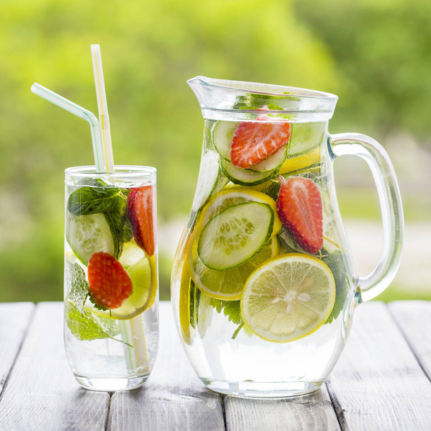 Dietary detox drink with lemon juice, red strawberry, cucumber and mint leaves in clear water with ice. - Foto, Imagen