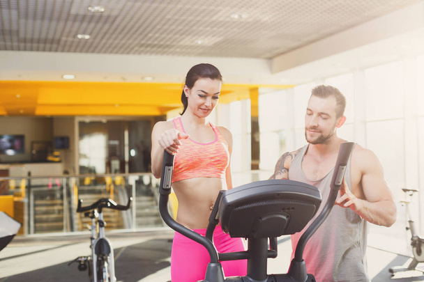 Fitness instructor helps young woman on elliptical trainer - Foto, Imagen