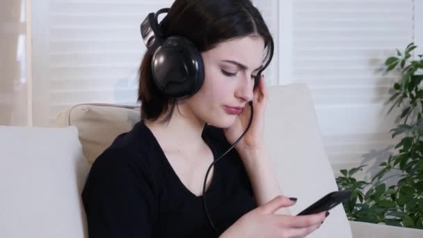 Beautiful attractive young woman sitting on sofa and listening to the music - Materiaali, video