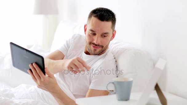 man with tablet pc drinking coffee in bed at home - Кадри, відео