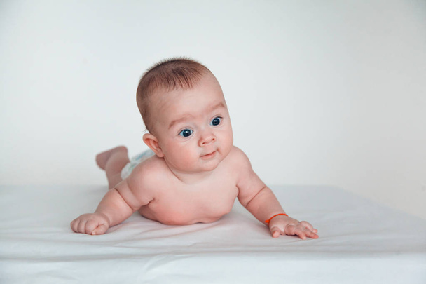 A funny baby with beautiful eyes lies on his stomach and smiles. - Photo, image
