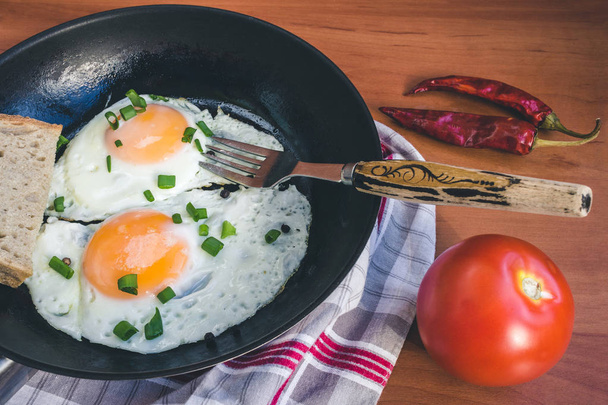 Gebakken eieren op pan, tomaat en chili peper op houten ondergrond. - Foto, afbeelding