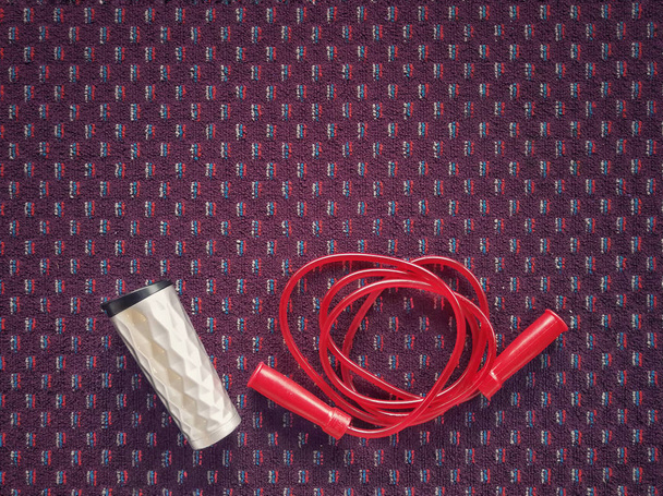 Water bottle and jumping red rope on a carpet floor at fitness gym. - Photo, Image