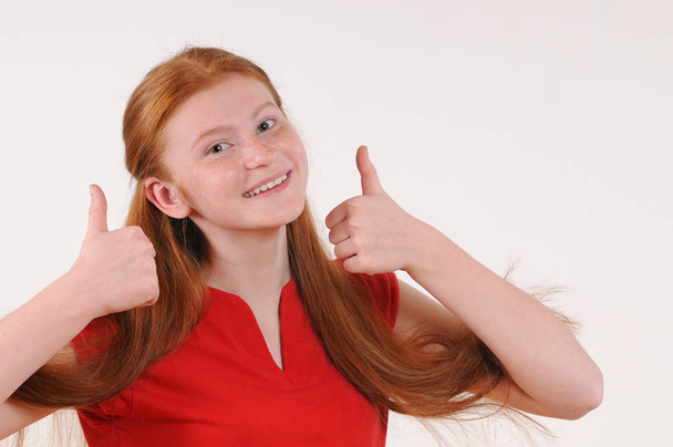 Menina tennager cabelo vermelho em uma camisa vermelha mostrando um polegar para cima em ambas as mãos
 - Foto, Imagem