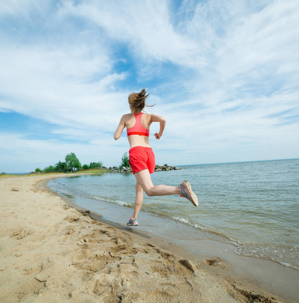 Young lady running at the sunny summer sand beach. Workout.  Jog - Фото, зображення