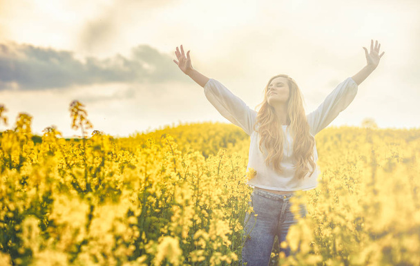 Happy smiling woman in yellow rapeseed field at sunset freedom concept - Fotó, kép