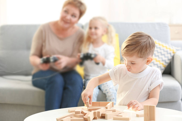 Cute little boy playing with wooden blocks while his sister and grandmother are immersed in video game - Zdjęcie, obraz