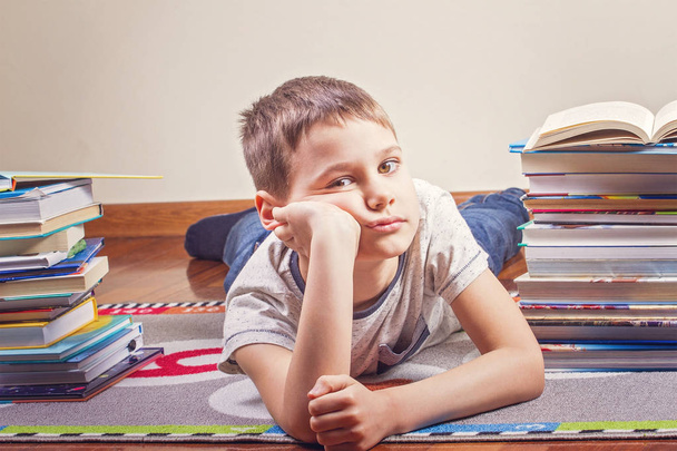 Скучный ребенок лежит между грудами книг
 - Фото, изображение