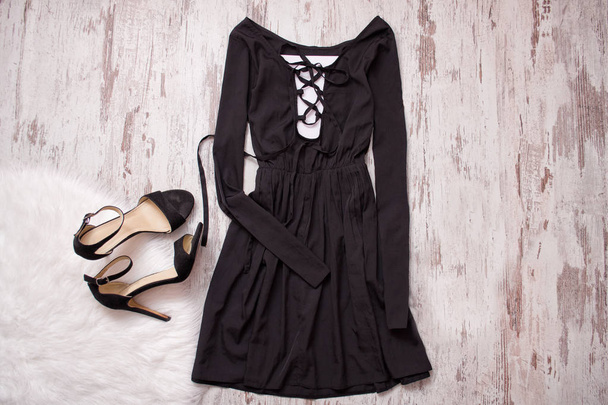 schwarzes Kleid mit langen Ärmeln und Binde, schwarze Schuhe. Holz Hintergrund, modisches Konzept - Foto, Bild