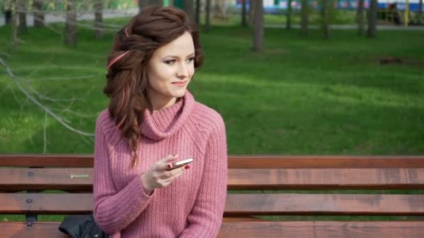 Gimbal shot of female teen girl talking on the phone sitting on bench in spring sunny day, uhd prores footage - Séquence, vidéo