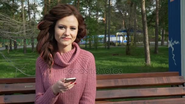 Prstenec záběr ženské dospívající dívka mluví o telefonu sedí na lavičce v jarní slunečný den, uhd prores záznam - Záběry, video