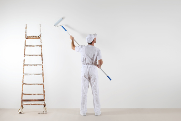 Vista trasera del pintor mirando a la pared en blanco, con palo de rodillo
 - Foto, imagen